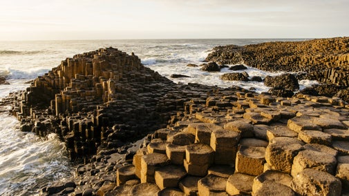 A coastline of geometrically shaped rocks with waves crashing against them